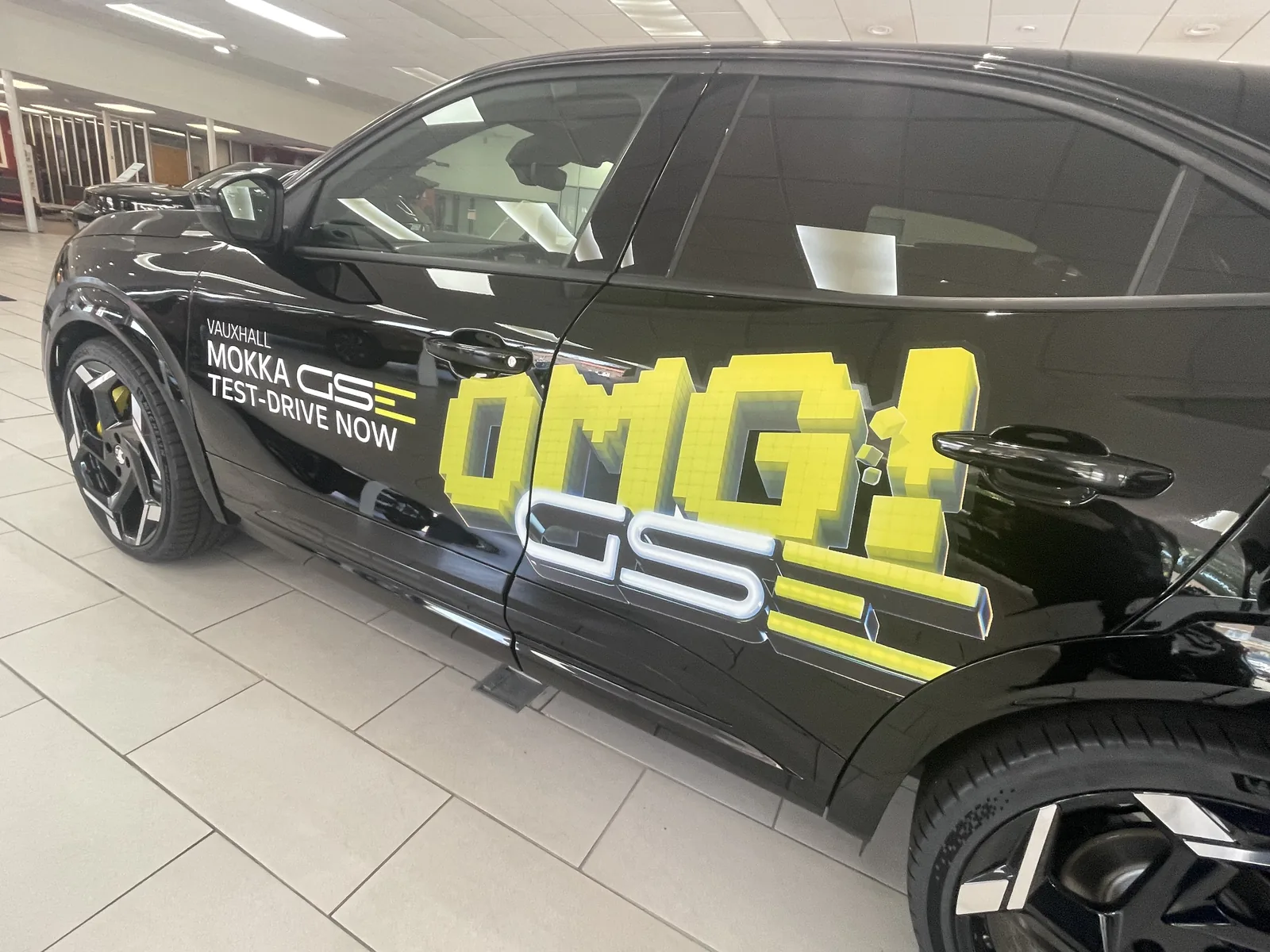 Bold yellow promotional graphics applied across the doors of a black car in a dealership showroom