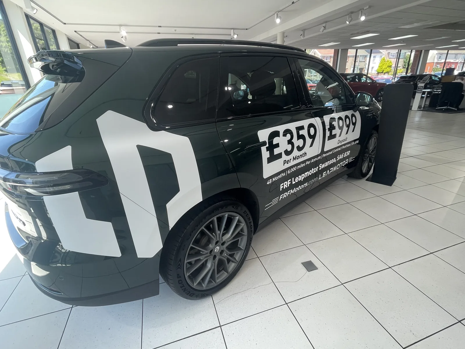Monthly price offer panel and a large white graphic applied to a black SUV in a dealership showroom